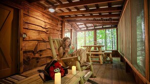 A rustic cabin interior with wooden walls, a wooden bench, a table with candles, and a view of the forest through large windows. - Lover's Nest at Saluda Grade Cabins! (Saluda)