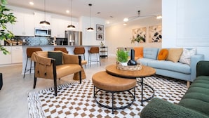 A modern living room with a sofa, chairs, and a coffee table. There is a kitchen in the background with white cabinets and a microwave. - Pro decor Disney Resort style FREE Waterpark 4467 (Kissimmee)