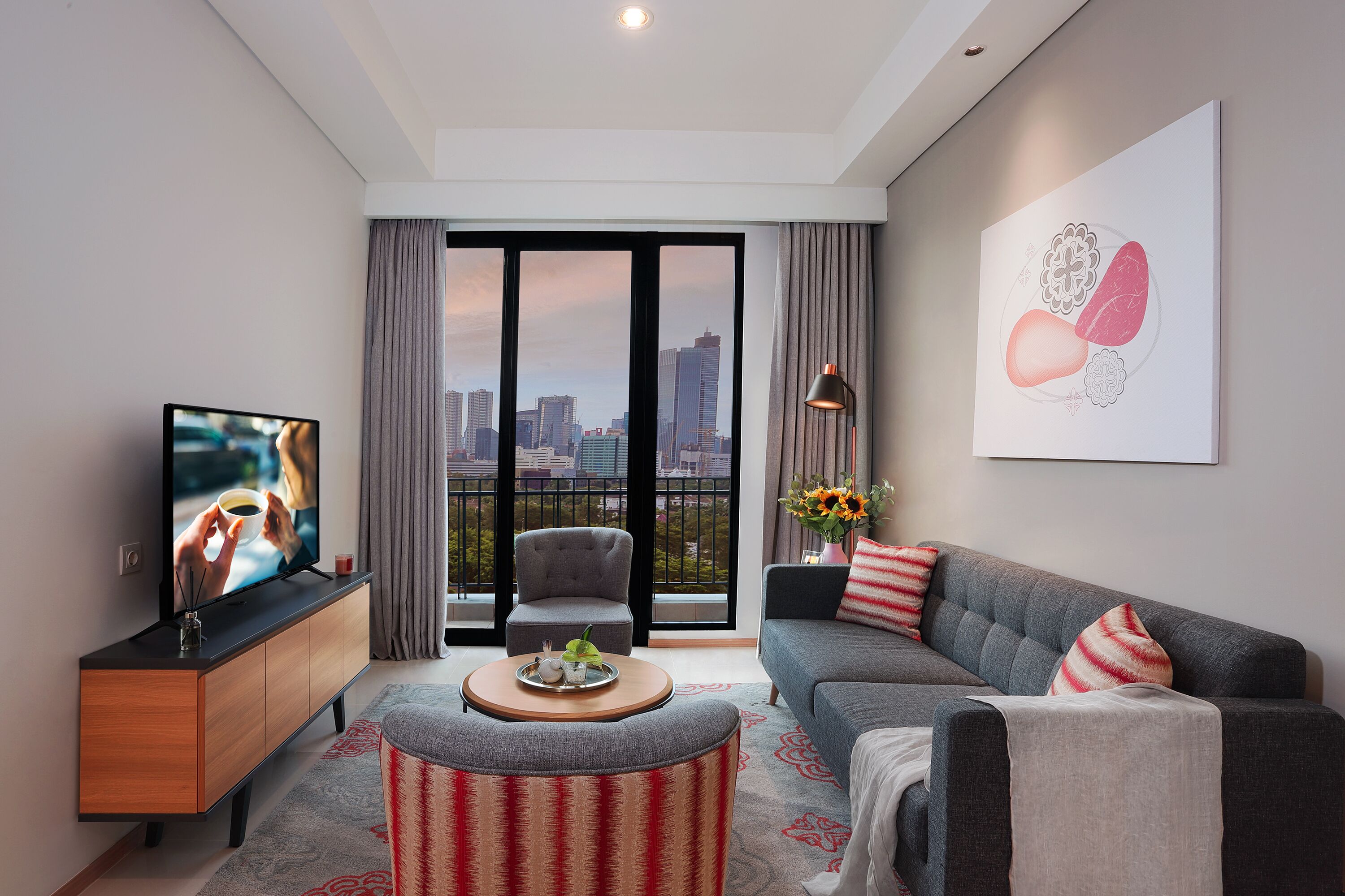 A modern living room with a television, sofa, and a balcony with a city view.