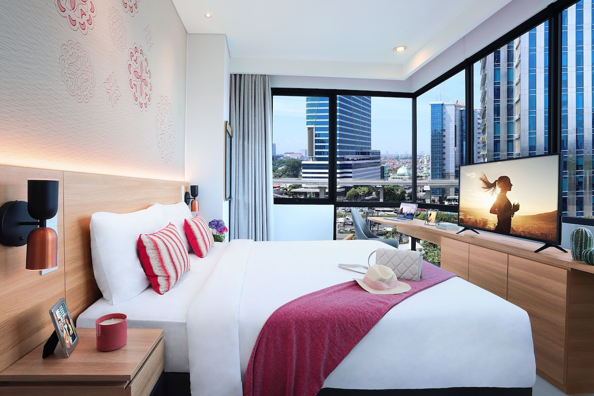 A modern hotel room with a large bed, a TV, and a city view.