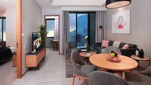 Ein modernes Hotelzimmer mit Essbereich, Fernseher, Sofa und großem Fenster mit Blick auf die Stadt.
