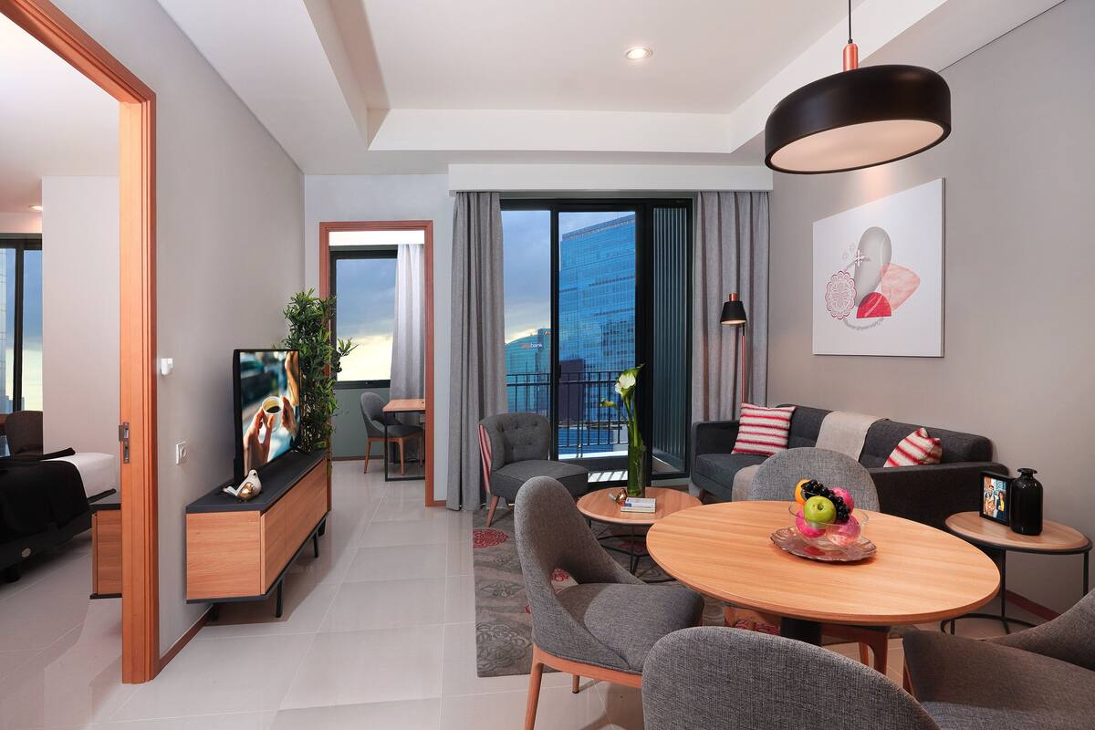 Ein modernes Hotelzimmer mit Essbereich, Fernseher, Sofa und großem Fenster mit Blick auf die Stadt.