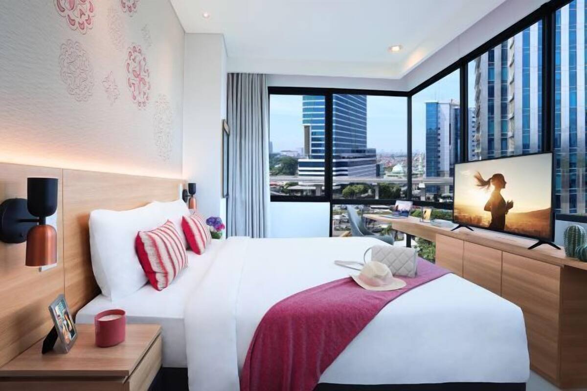 Ein modernes Hotelzimmer mit einem großen Bett, einem Fernseher und Blick auf die Stadt.