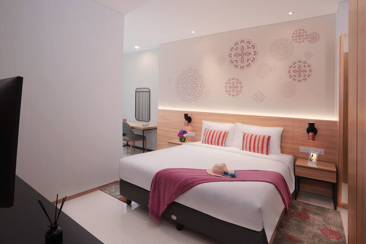 Ein modernes Hotelzimmer mit einem großen Bett, einem Schreibtisch, einem Sessel und einem Fernseher.