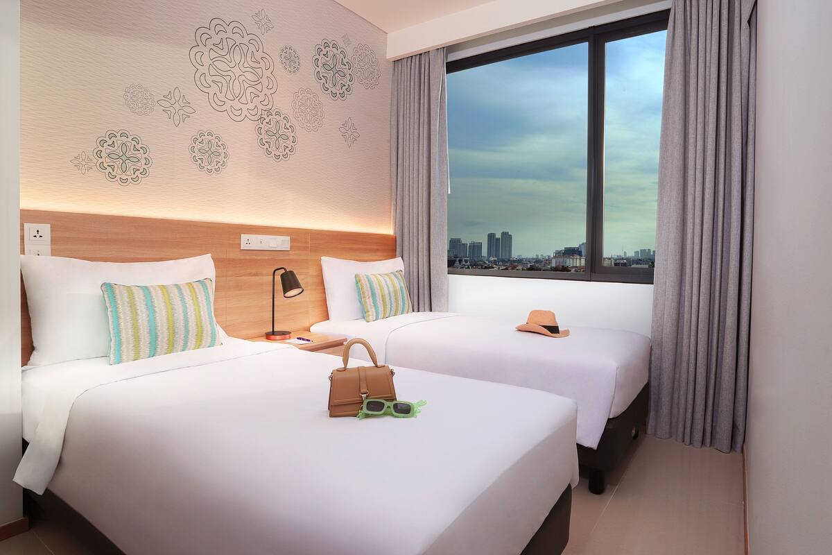 Ein Hotelzimmer mit zwei Betten, Blick auf die Stadt und einer Wandverzierung.