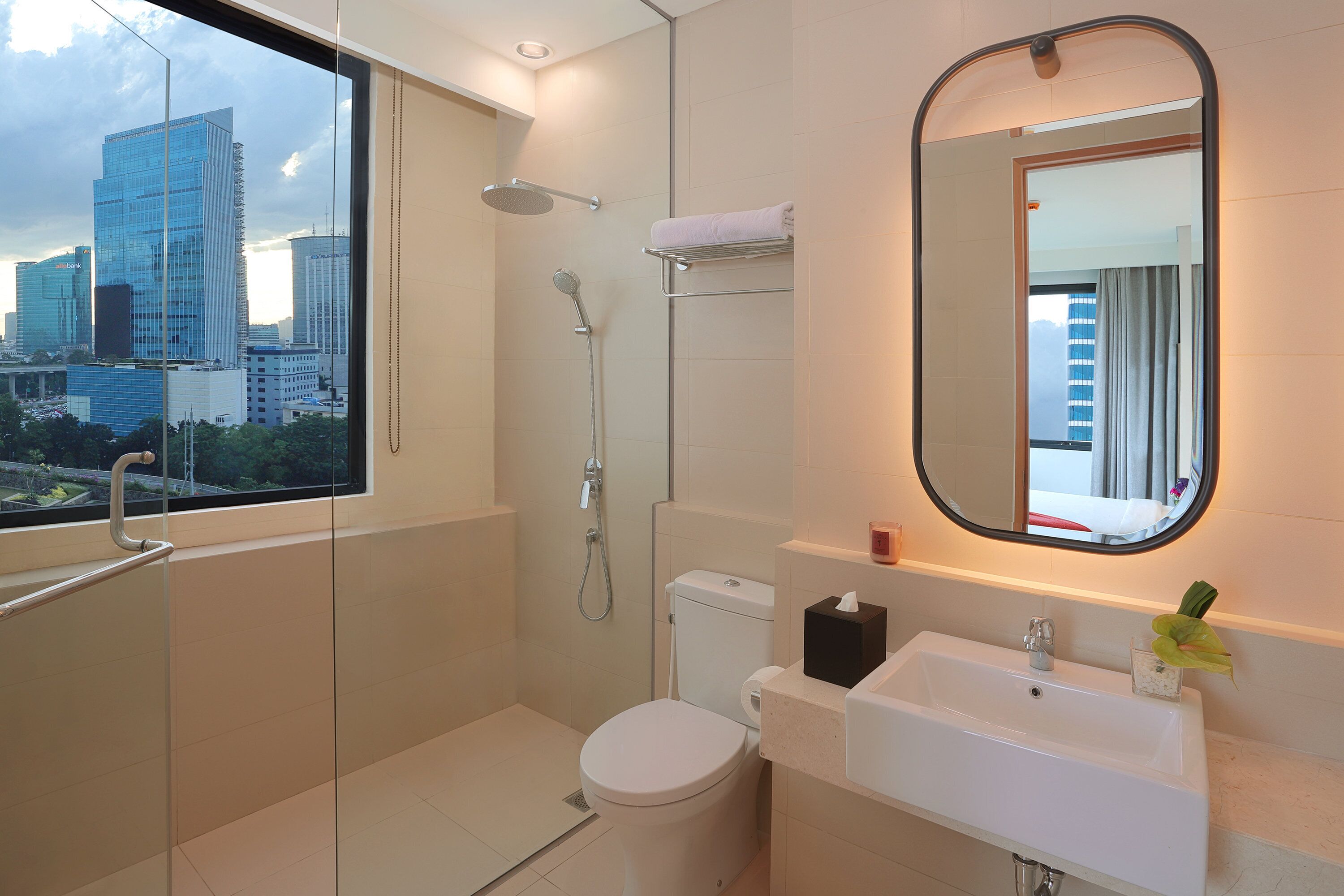 Een moderne badkamer met toilet, wastafel en douche. Een raam biedt uitzicht op de stad.