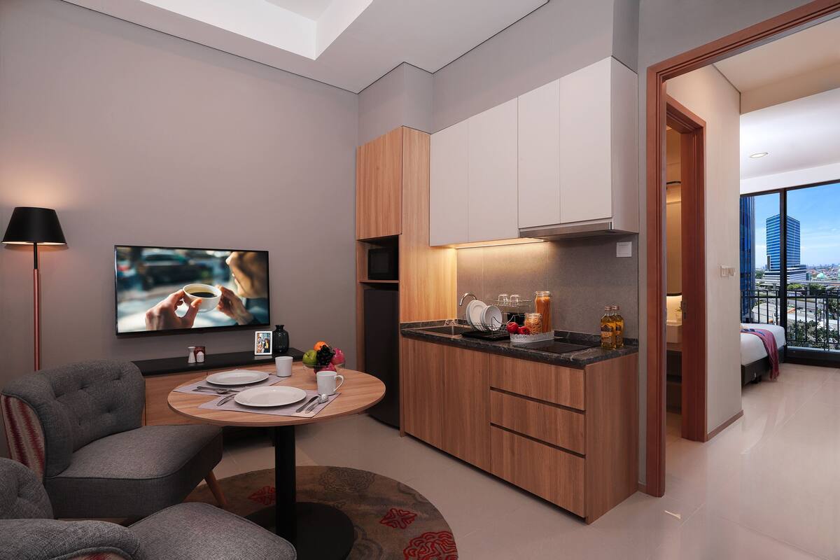 Eine moderne Küche mit Holzausstattung, ein Essbereich mit rundem Tisch und ein Fernseher, der eine Szene zeigt.