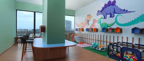 Zona de juegos para niños con un mural de dinosaurios, un corralito y vistas a la ciudad.