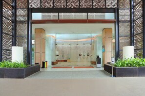 Een moderne hotelentree met een decoratief gevelontwerp, een receptiebalie en een glazen deur.