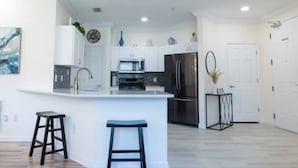 A modern kitchen with white cabinetry, a central island with stools, stainless steel appliances, and a decorative mirror. - Beautiful Luxury Condo (Davenport)