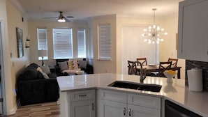 A modern kitchen with white cabinets, a black countertop, and a dining area with wooden chairs and a chandelier. - Beautiful Luxury Condo (Davenport)