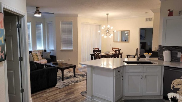 A modern kitchen with white cabinetry, a central island, and a dining area with a chandelier. - Beautiful Luxury Condo (Davenport)