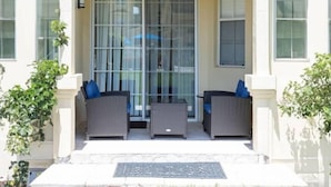 A covered outdoor seating area with wicker furniture and a glass door. - Beautiful Luxury Condo (Davenport)