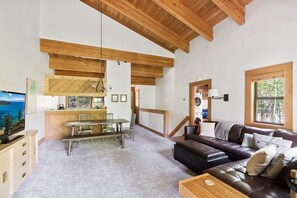 The view over the open main living space, a charming area with high ceilings, exposed wood beams, and views over the trees from the large windows.