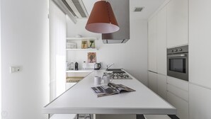 A modern kitchen with white cabinetry, a central island with a magazine, a stainless steel oven, and a pendant light. - Italianway Comfort - Palestrina 31 (Milan)