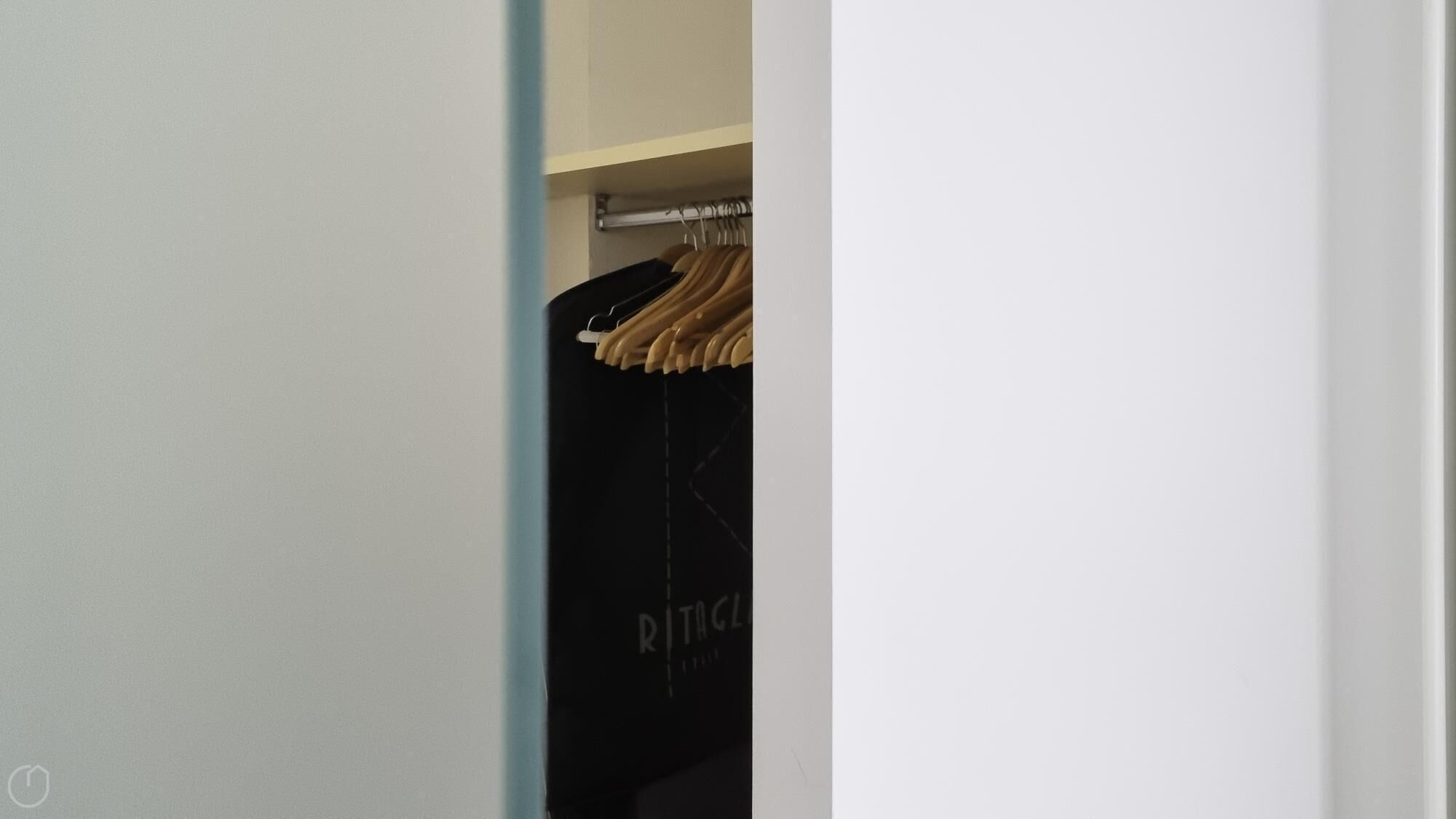 Un placard contenant des vêtements suspendus et un sac noir sur lequel on peut lire le mot « RITAGL ».