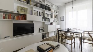 A modern living room with a flat-screen TV, bookshelves, a dining table with chairs, and a large window. - Italianway Comfort - Palestrina 31 (Milan)