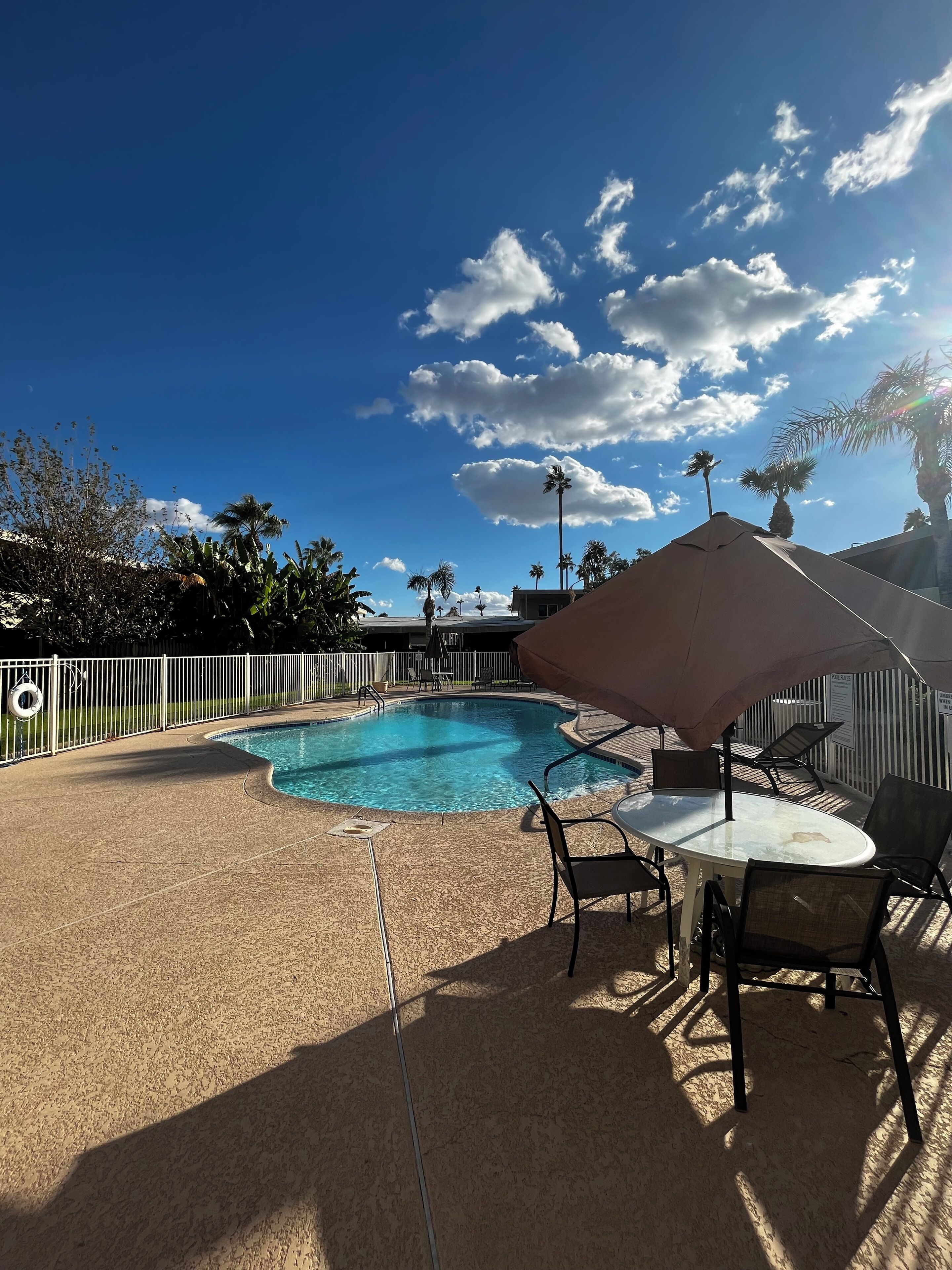 A swimming pool with a surrounding patio area, including a table and chairs, and a large umbrella providing shade.