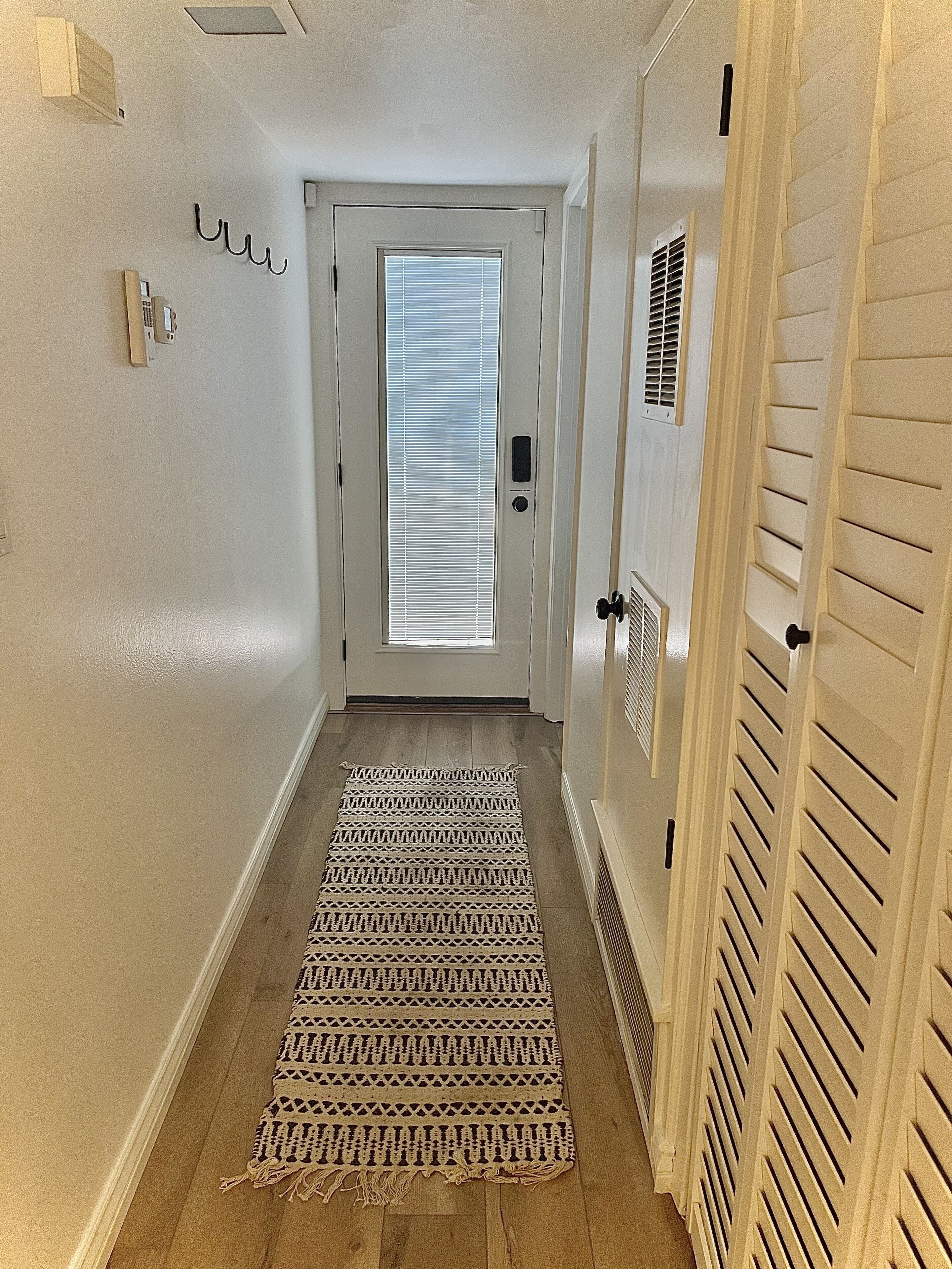 Un couloir avec un tapis à motifs, une porte dotée d’une fenêtre et un thermostat fixé au mur.