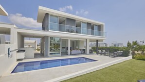 Uma casa moderna de dois andares com piscina, área de estar externa e uma grande varanda de vidro.