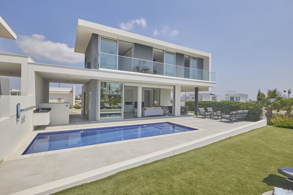 A modern two-story house with a swimming pool, outdoor seating, and a large glass balcony.