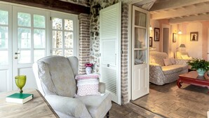 A cozy living room with a stone wall, a large armchair, a sofa, and a wooden coffee table. - Podere San Giorgio 6 Emma Villas (Manciano)