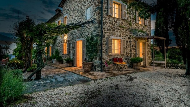 A stone house with multiple windows and doors, surrounded by greenery and a gravel path. - Podere San Giorgio 6 Emma Villas (Manciano)
