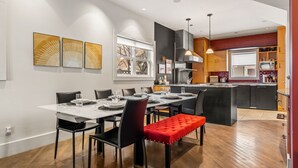 Un espace repas moderne avec une grande table dressée pour six personnes, entourée de chaises noires et d’un banc rouge.