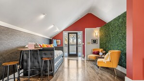 Il s’agit d’une chambre moderne de style « loft », avec un plafond haut, un mur en pierre, un mur végétal et un plancher en bois. On y trouve un lit avec une tête de lit grise, un bureau avec une chaise et un fauteuil jaune.