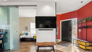 Un salon moderne avec un téléviseur à écran plat, un banc, une bibliothèque et un mur d’accent de couleur rouge.