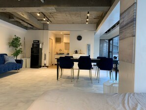 A modern living space with a dining area, kitchen, and a large window providing natural light. - Spacious Studio West Shinjuku (Tokyo)