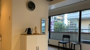 Una habitación con un armario blanco, un reloj y dos sillas junto a un ventanal con vistas a edificios.