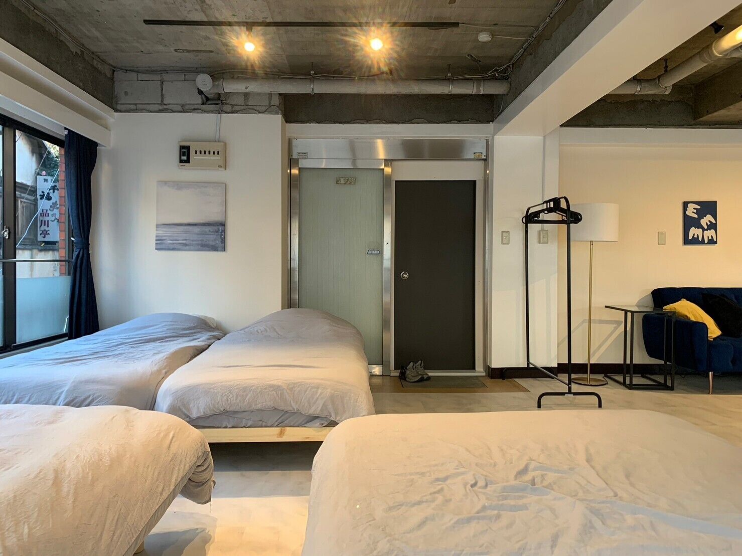 Habitación de hotel con dos camas, una puerta, perchero y lámpara.