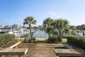 A wooden deck with benches overlooking a marina with boats and palm trees.