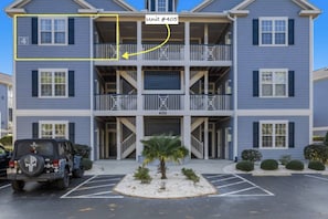 A multi-story residential building with balconies, a parking lot, and a Jeep parked in front.