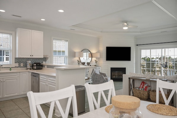 A modern kitchen with white cabinetry, a central island, and a dining area with white chairs.