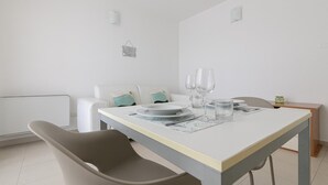 A dining area with a table set for two, featuring a white tablecloth, two plates, two glasses, and a small jar.