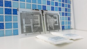 Two packages of Intimate Cleanser labeled 'Hotel Excelsior' in a bathroom with blue mosaic tiles.