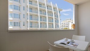 A balcony with a view of a white building with multiple balconies and windows. There is a small table with a teapot, cup, and magazine.