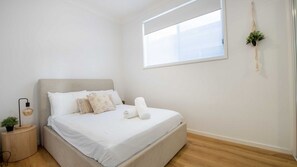 A minimalist bedroom with a bed, bedside table, lamp, and a hanging plant.