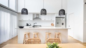 A modern kitchen with white cabinets, a central island with stools, and black hanging pendant lights. - Surfleet Serenity is a coastal duplex (Kiama)