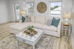 A living room with a light-colored sectional sofa, a checkered coffee table, and a round wall decoration.