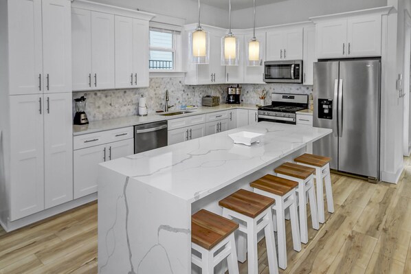 A modern kitchen with white cabinetry, a central island with stools, stainless steel appliances, and pendant lighting.