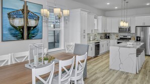 A modern kitchen with white cabinetry, a wooden dining table, and a large island. - Private *Heated Pool | Free Golf Cart | New Home | Patio Area | 5 Outdoor Spaces | Game Table (Santa Rosa Beach)