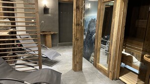 Una sauna amb bigues de fusta, zona de seients i un mural gran a la paret amb un paisatge de muntanya.