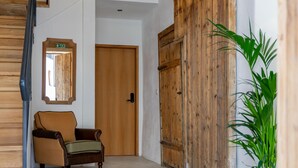 Un passadís amb una porta de fusta, una cadira i una planta en test.