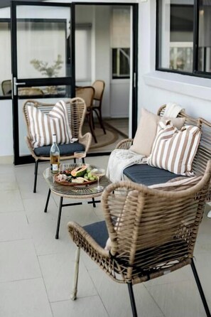 A room with wicker furniture, a dining table with food, and a sliding glass door leading to an outdoor area. - Pia's Paradise Kiama (Kiama)