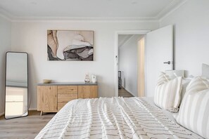 A bedroom with a bed, a wooden dresser, a mirror, and a painting on the wall.