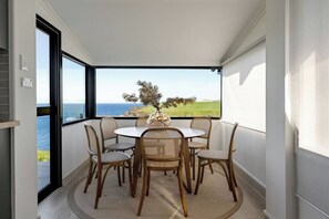 A balcony with a round table and six wicker chairs, overlooking a coastal landscape.