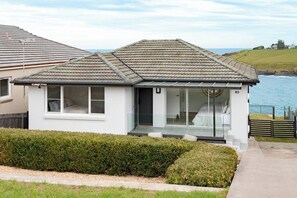 A modern house with a tiled roof, large windows, and a view of the sea.